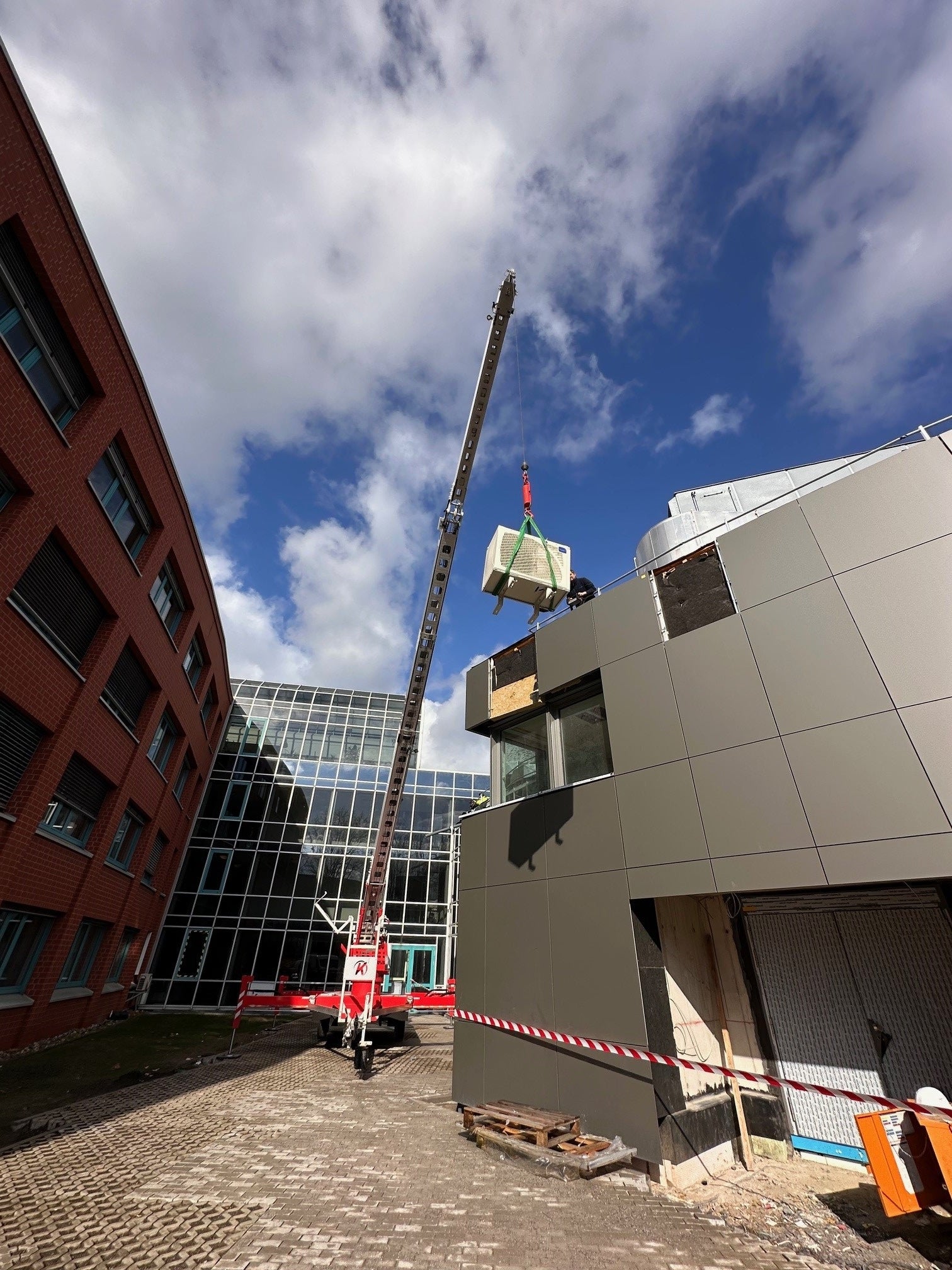 Ein Kran hebt ein professionelles Küchengerät auf ein Dach, damit eine neue Produktionsküche eingebaut werden kann