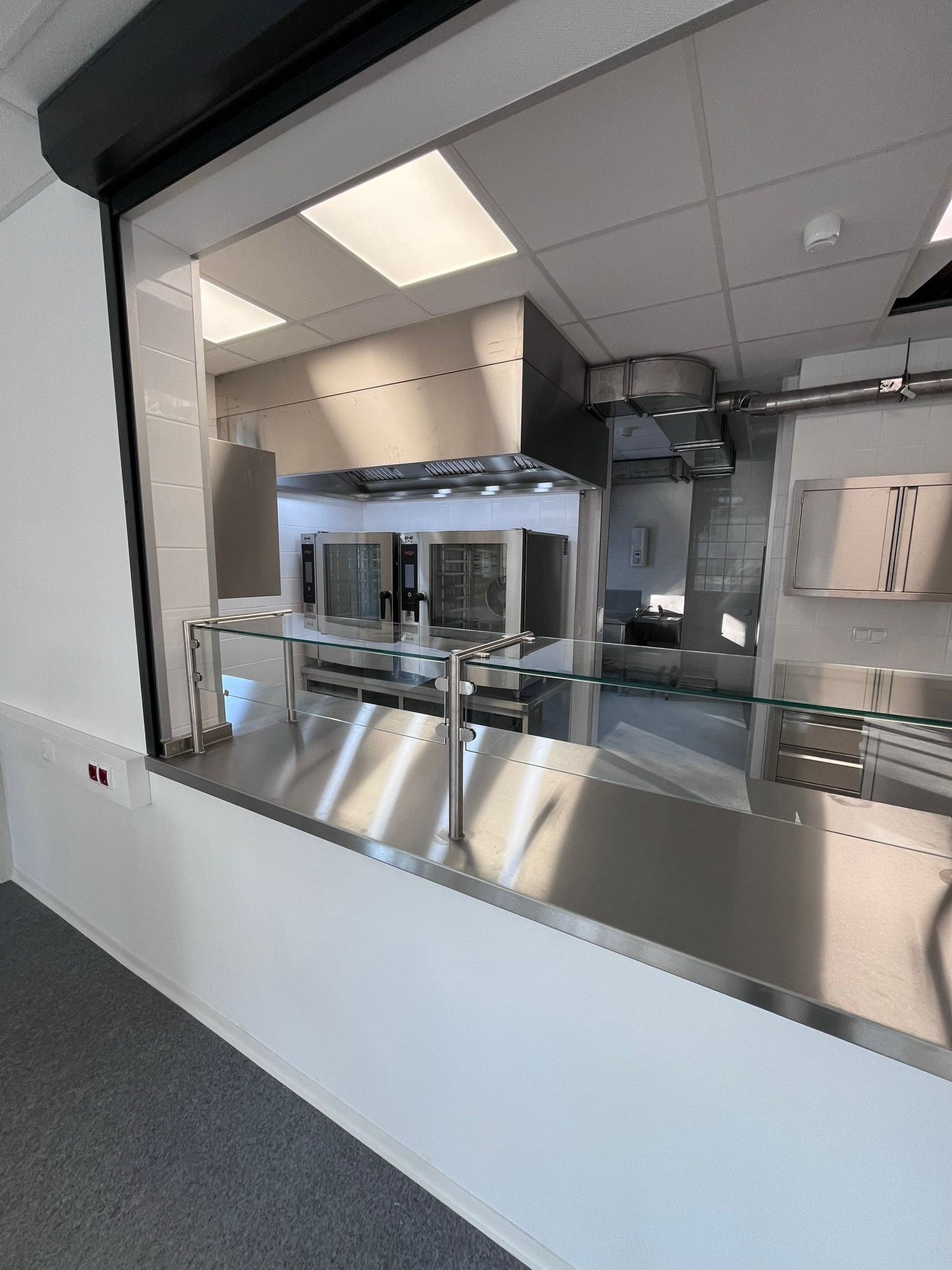 Eine von TIMMER individuell gefertigte Ausgabetheke aus Edelstahl mit einer neuen Systemküche im Hintergrund